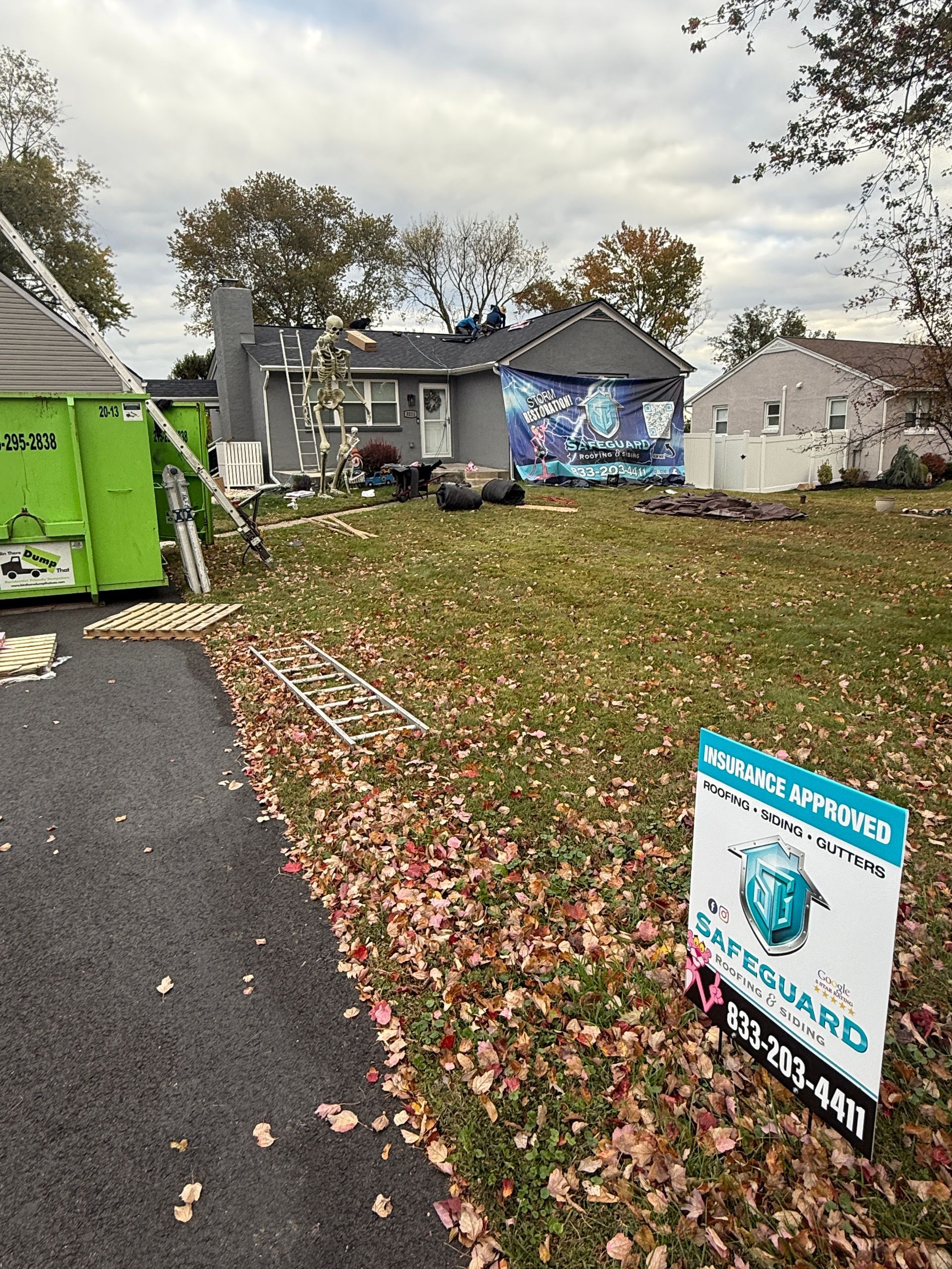 House under construction with green dumpster, yard with fall leaves. Sign in foreground.