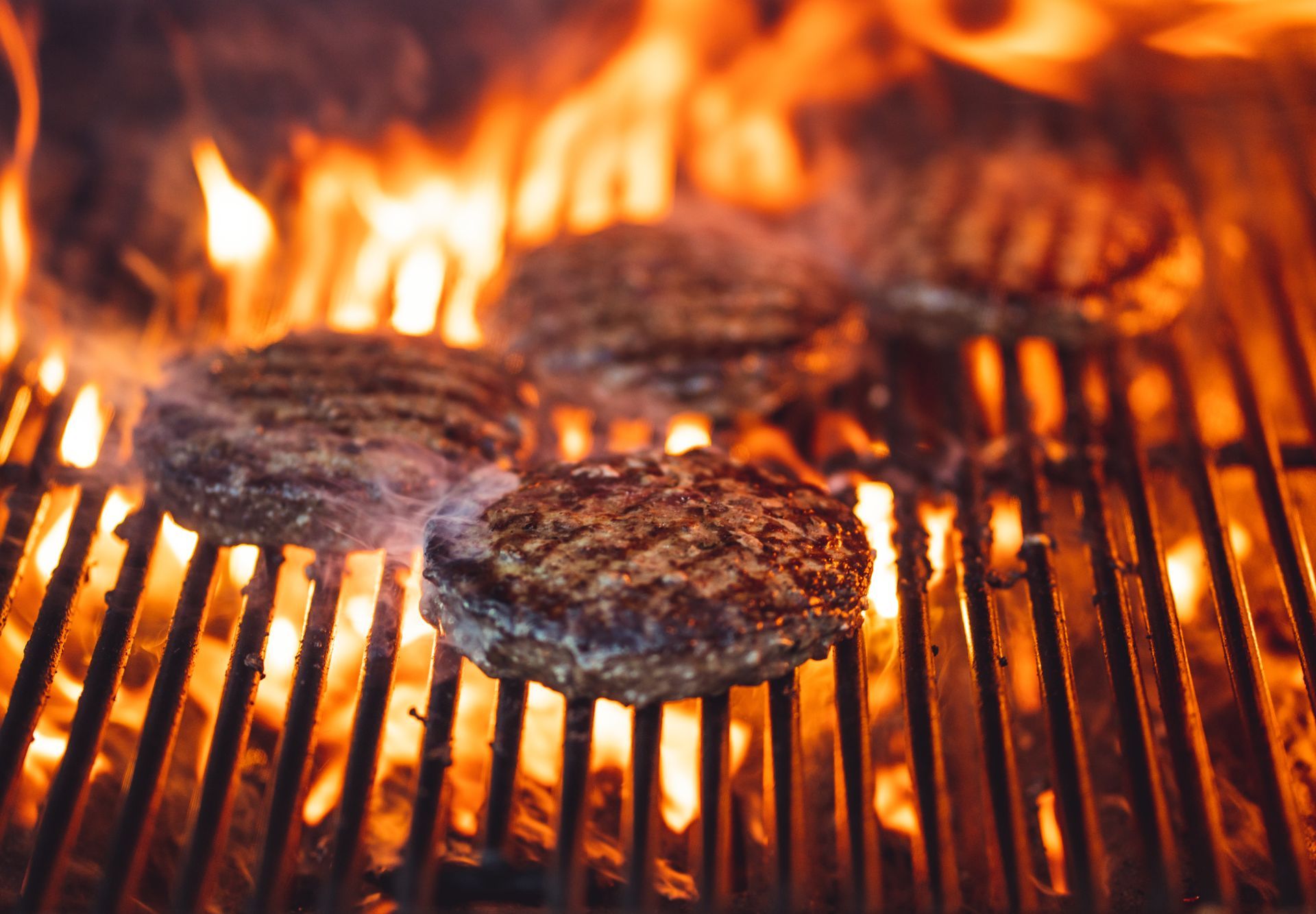 Burgers being flame grilled on a BBQ.