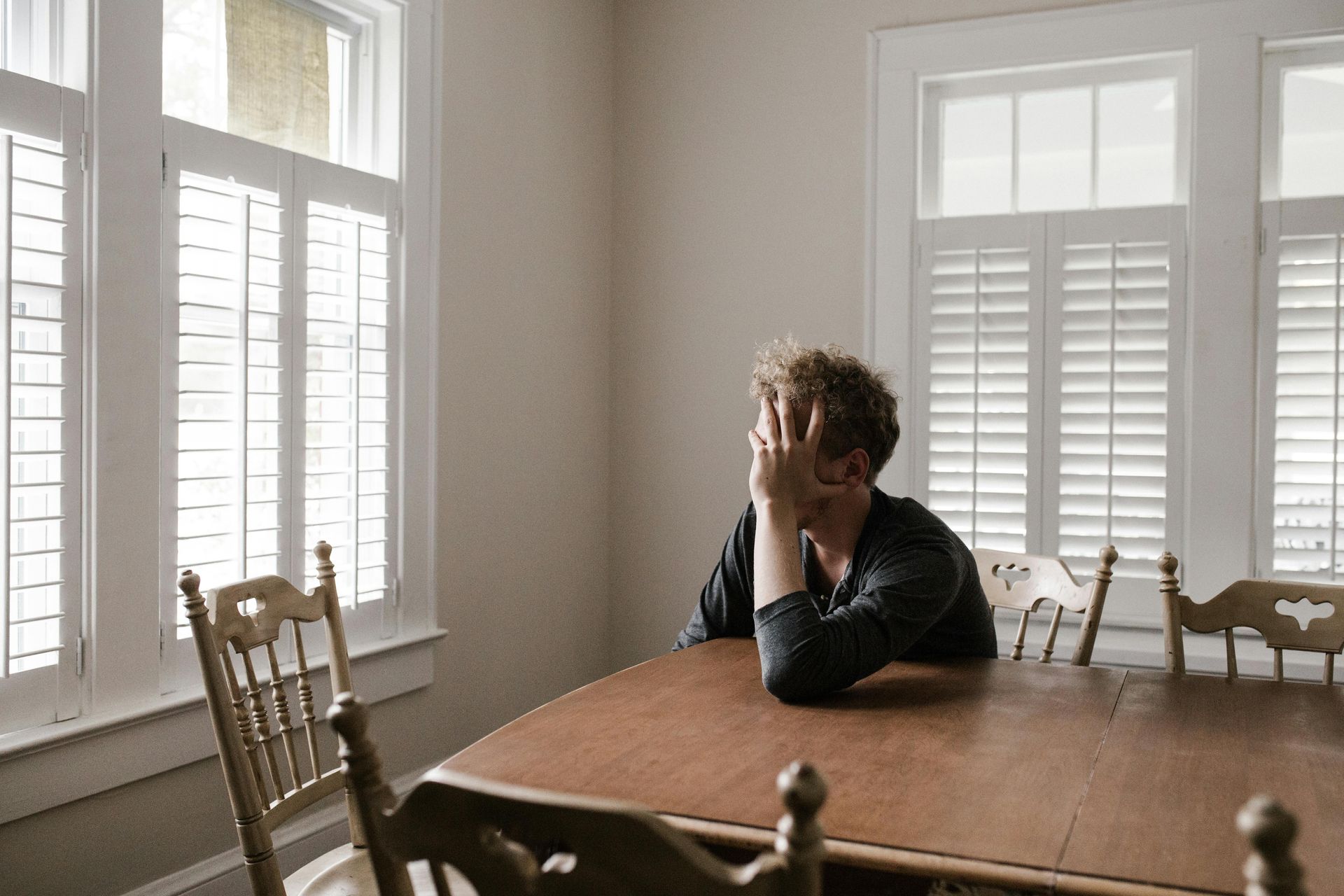 man sits at a wooden table looking out the window contemplating news of partner's abortion
