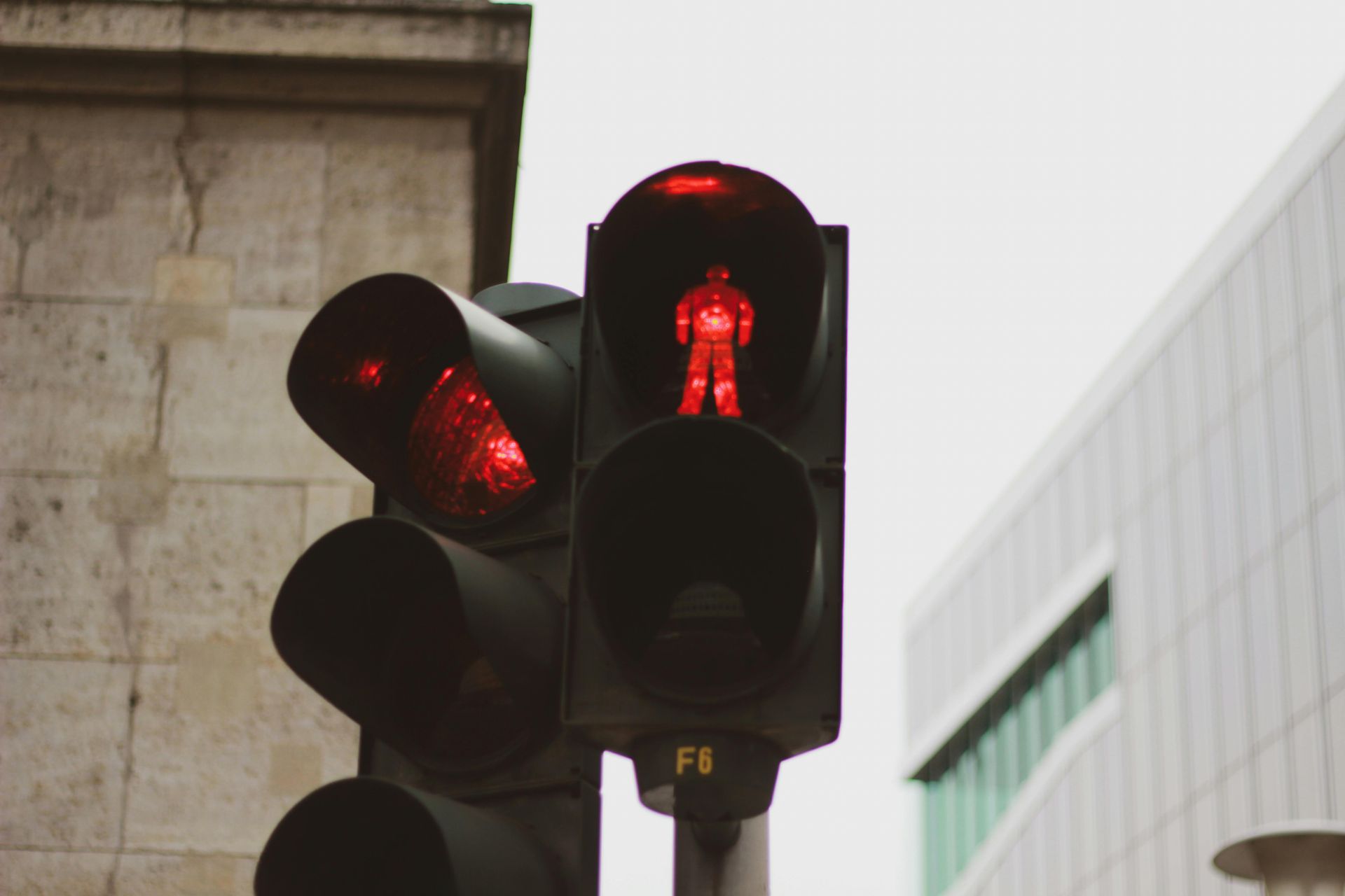 Close-up of a pedestrian traffic light showing a red figure against a blurred city backdrop