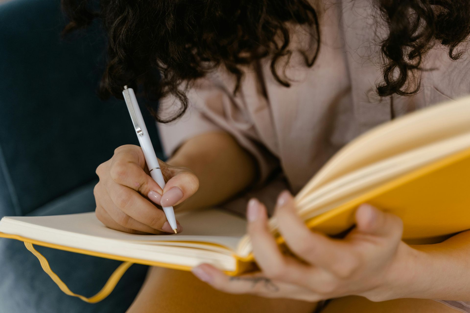 Hands holding a yellow journal and pen, mid-writing, in a peaceful and personal moment.