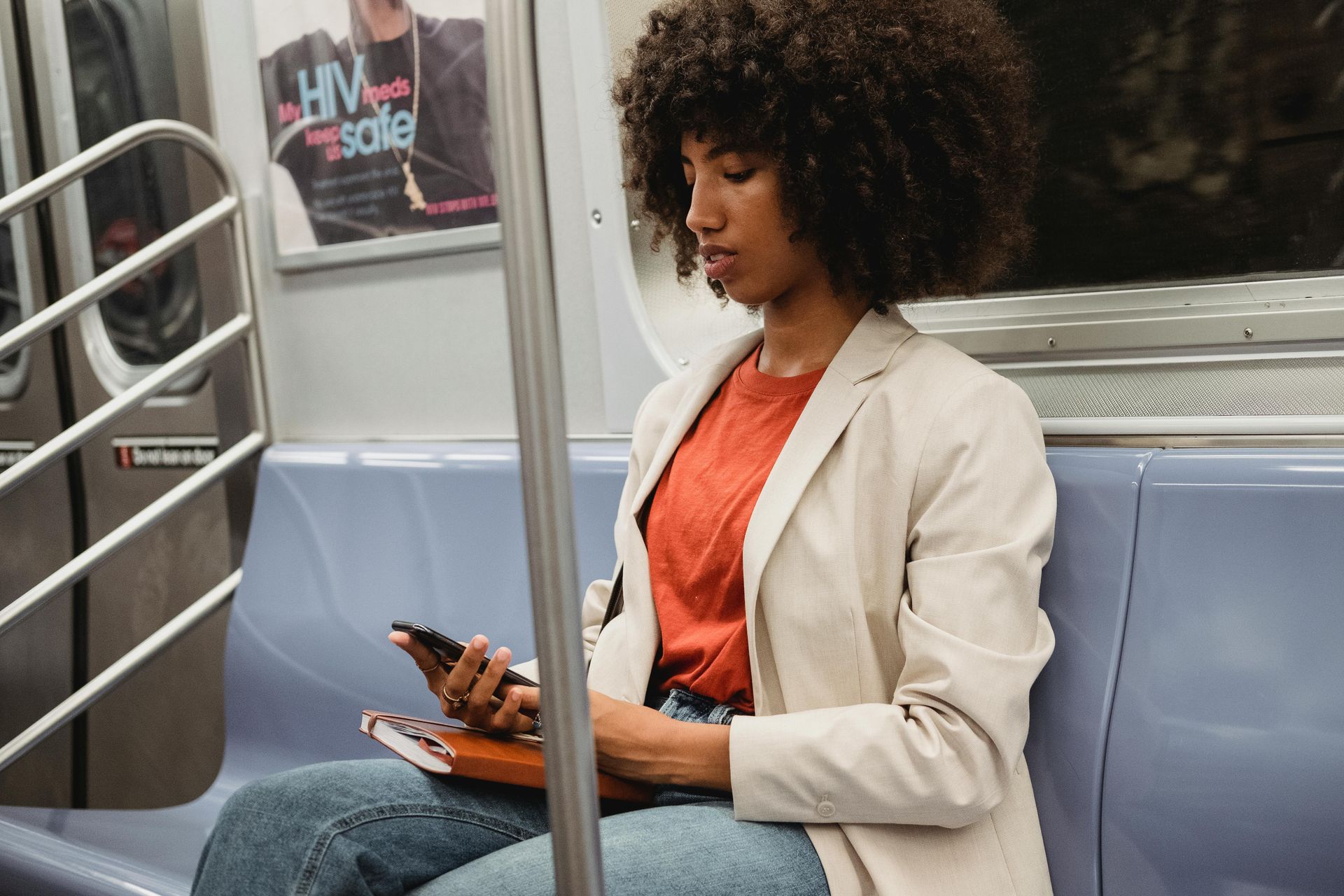 black woman on NYC subway on her phone with a red notebook