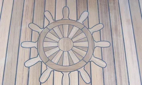 Ship's wheel embedded in a teak decking design, showcasing intricate craftsmanship and nautical elegance on a yacht