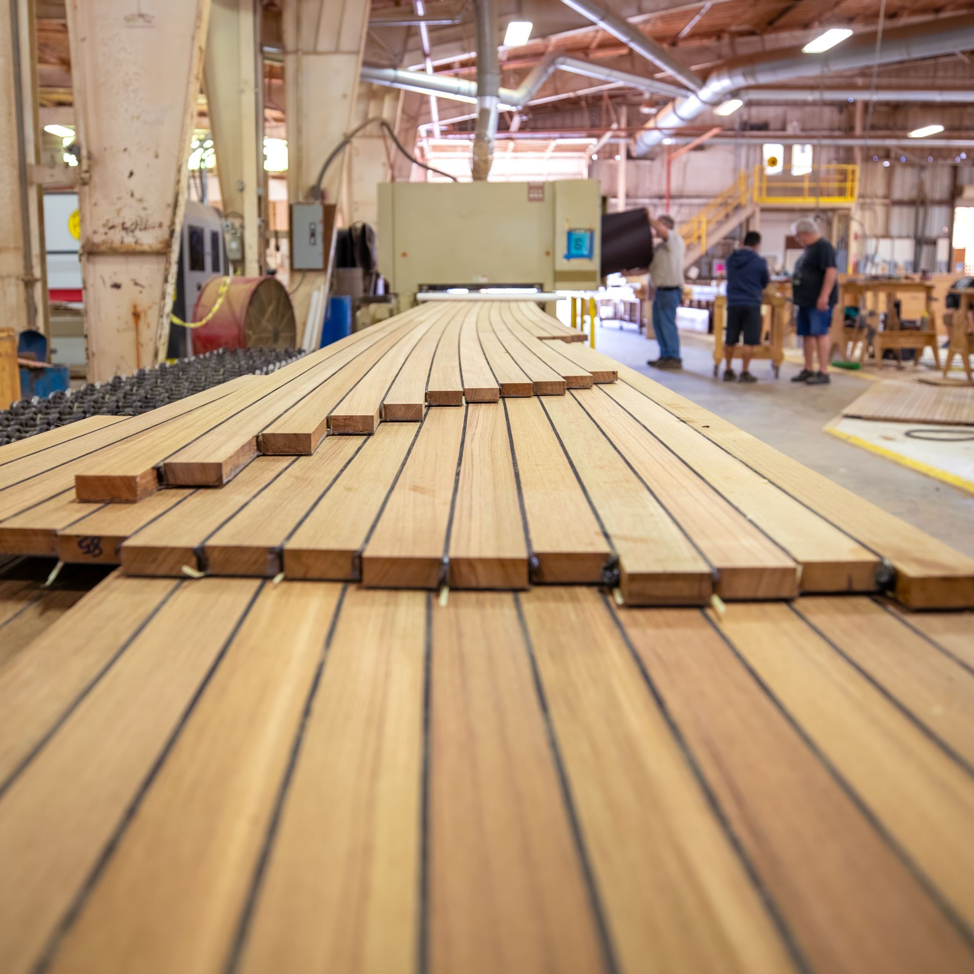 Teak wood emerging smoothly from a sanding machine at Teakdecking Systems, showcasing a refined and polished surface