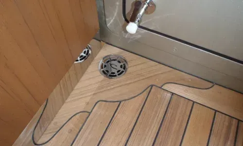 Teak decking on a yacht by Teakdecking Systems, featuring a perfectly crafted seam around a corner, enclosing a drain
