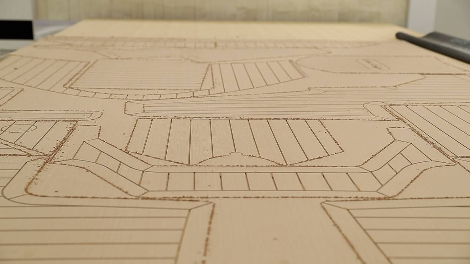Close-up of a CNC-routed board showing detailed decking pattern cuts with grooves and curved edges on a wooden surface.