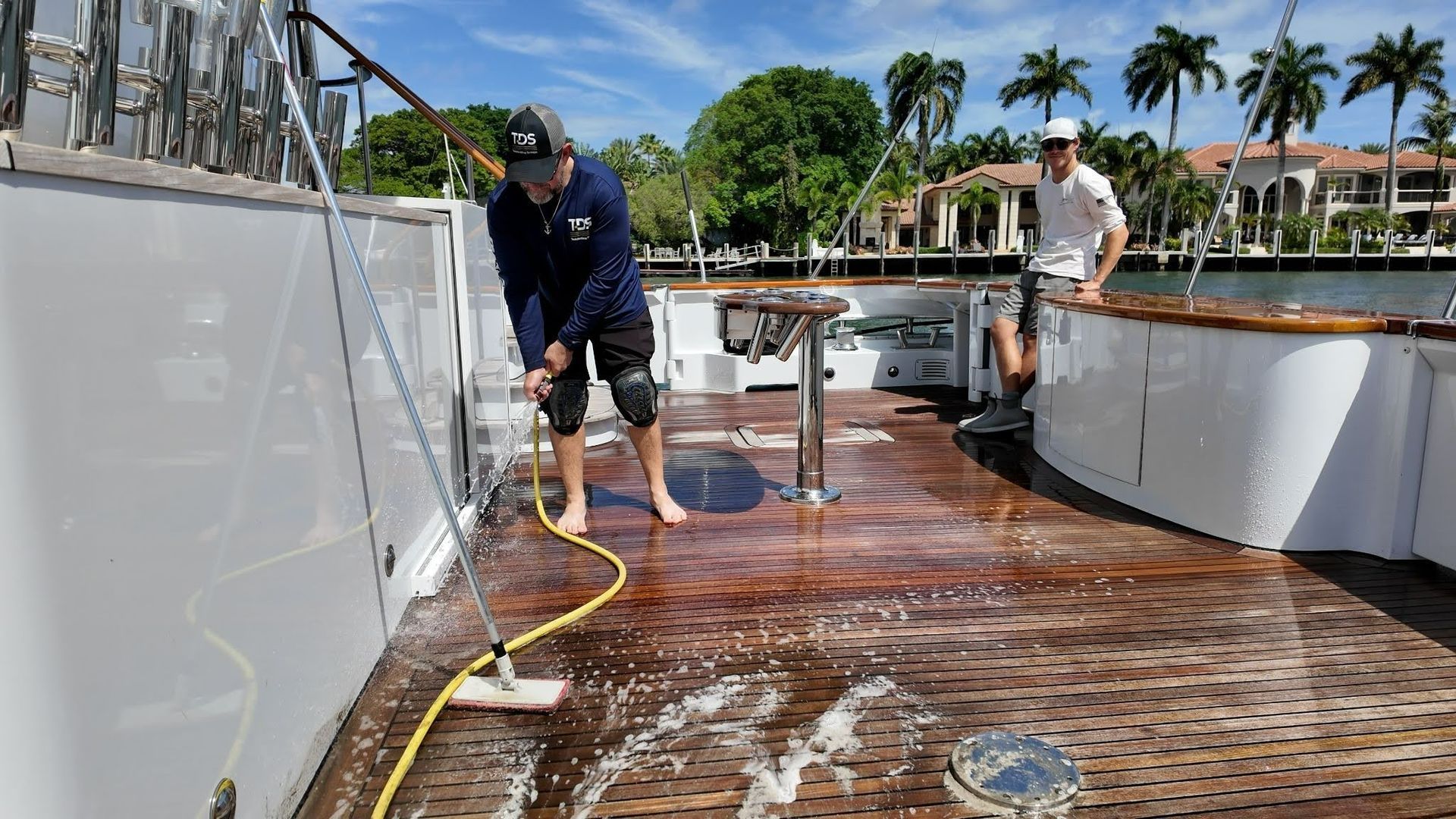 TDS technician cleaning a yacht’s teak deck with ECO-friendly foam cleaner and deck brush while dock