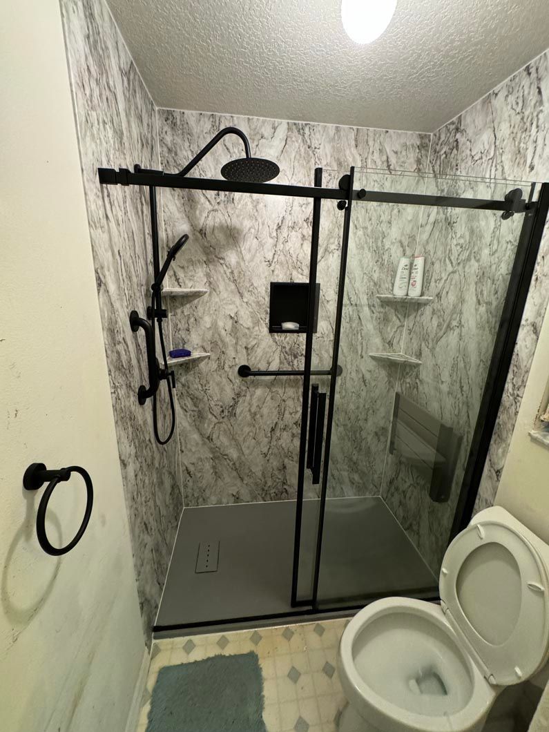A bathroom with a toilet , shower , and sliding glass door.