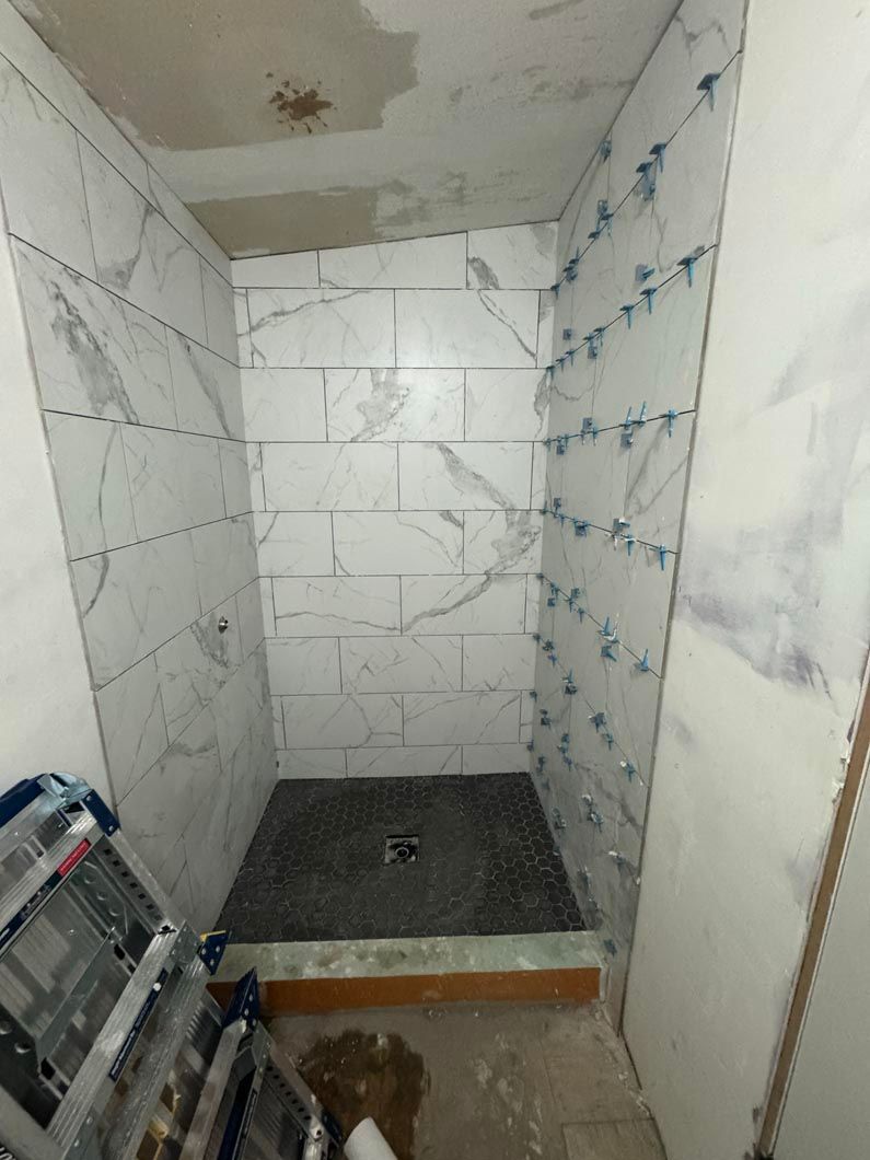 A bathroom under construction with a shower stall and a ladder.