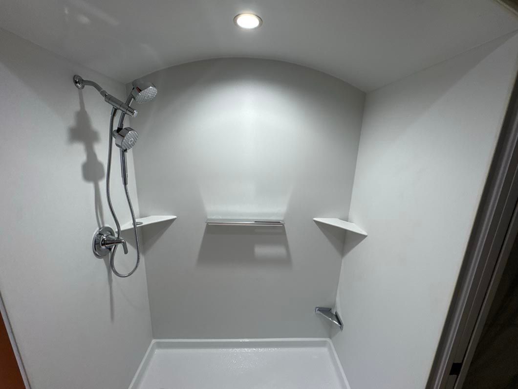 A shower with a shower head and shelves in a bathroom.
