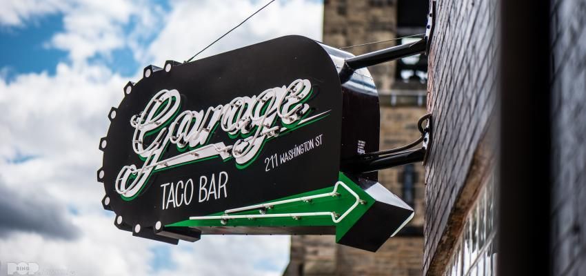 A sign for a taco bar is hanging from the side of a building.