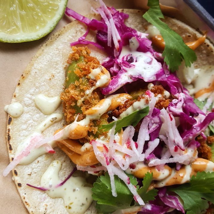 A close up of a taco with a lime in the background.