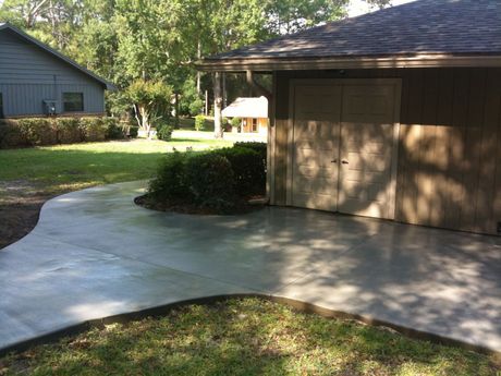 A concrete walkway leading to a garage with a house in the background