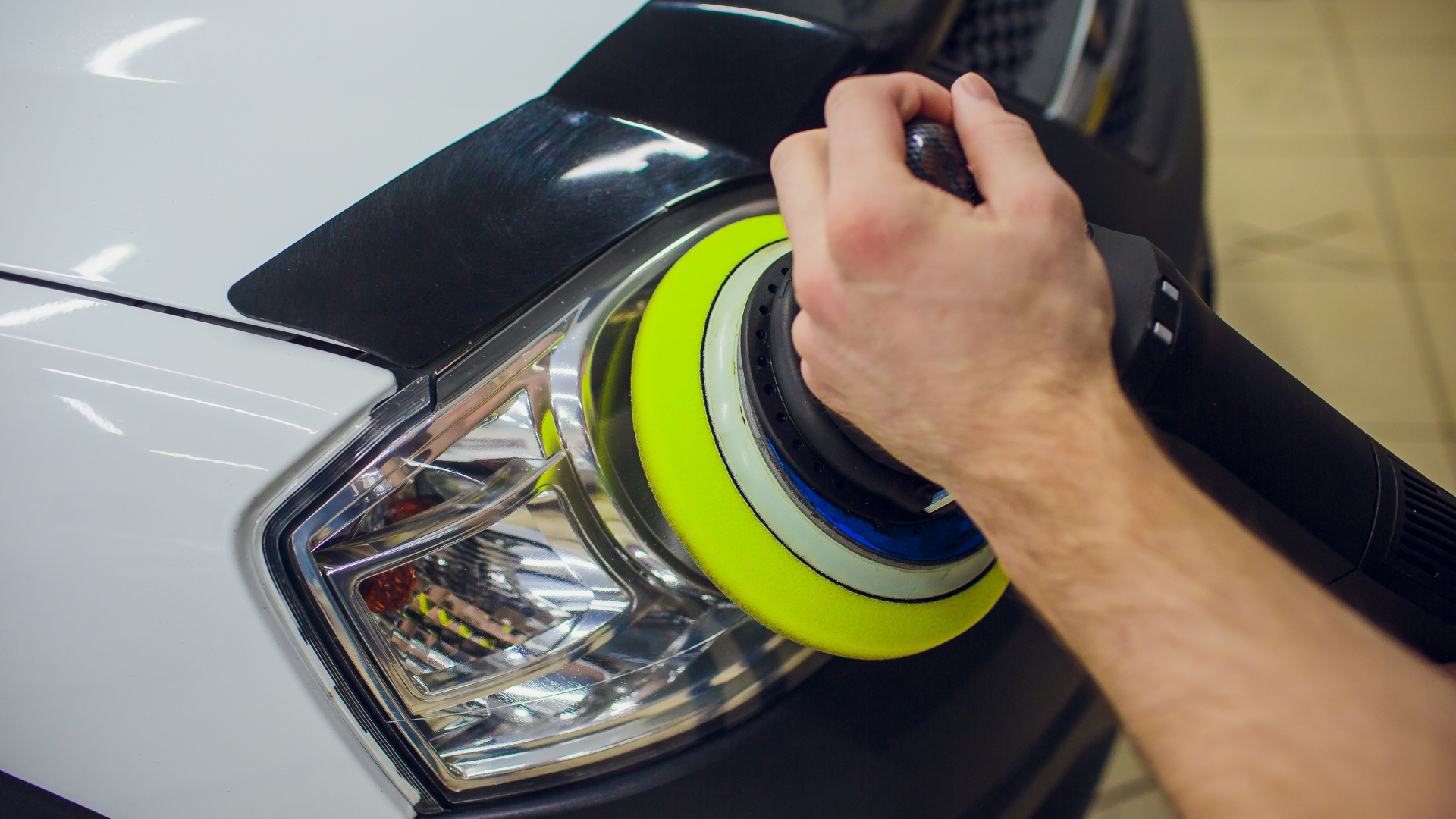 A person is polishing a car headlight with a yellow polisher.