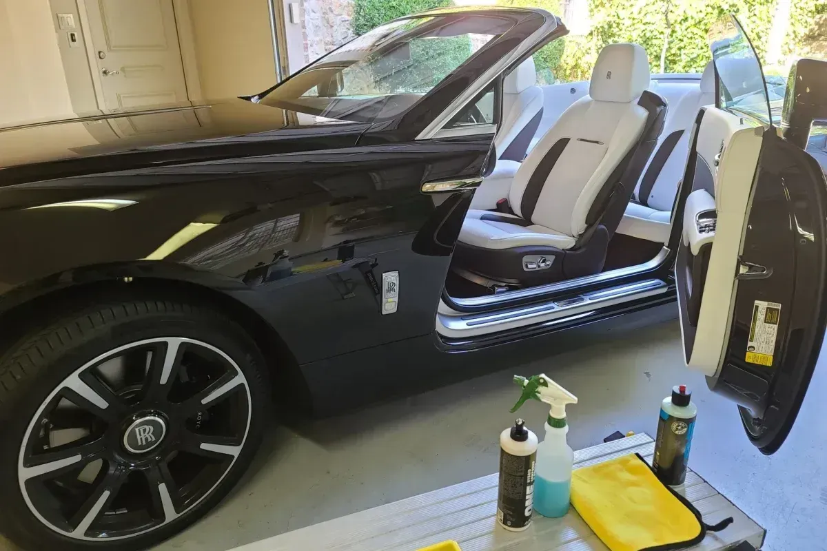 A black convertible car is parked in a garage with its doors open.