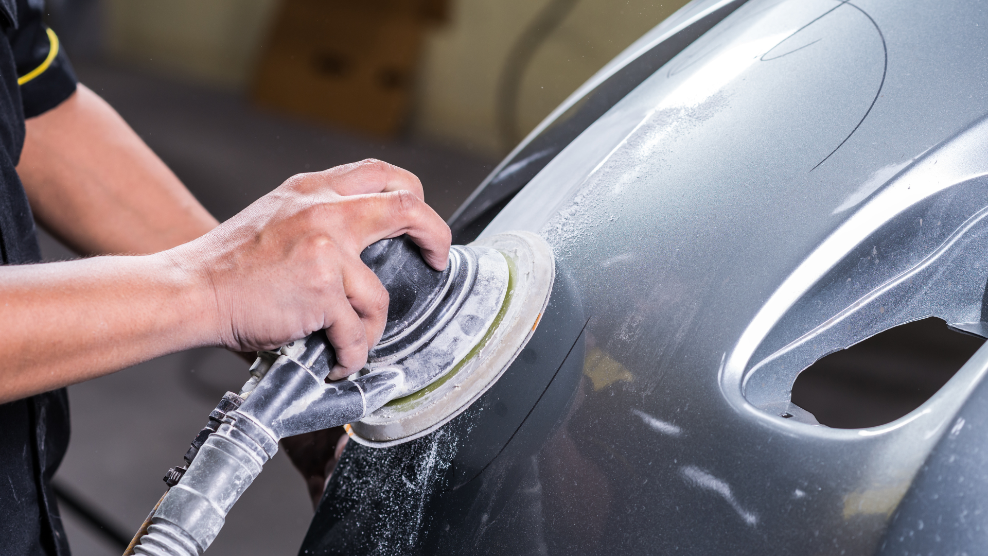 A man is sanding a car bumper with a sander.