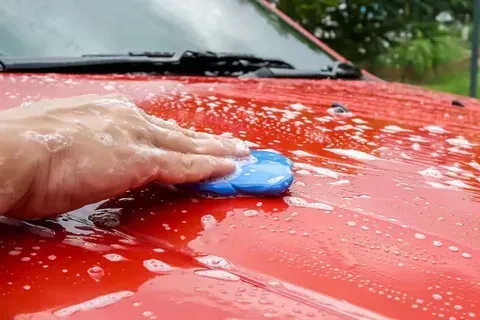 A person is washing a red car with a blue sponge.