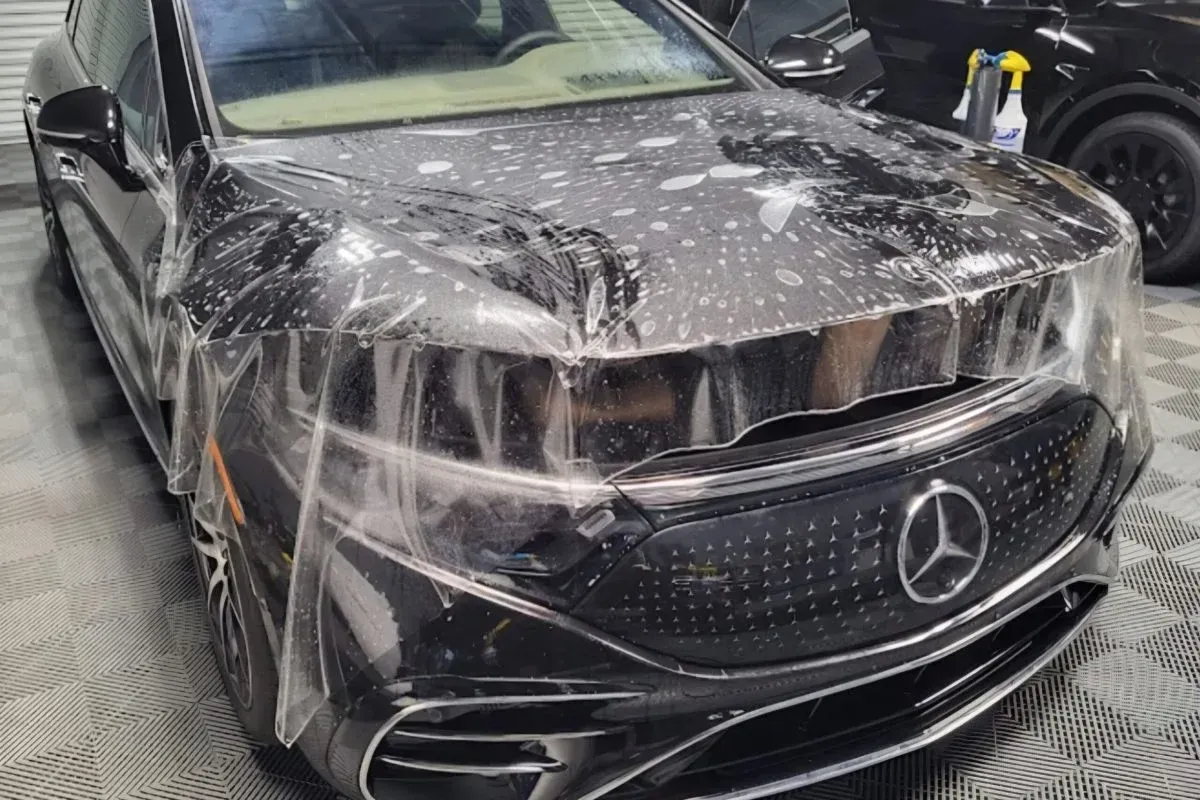 A black mercedes benz is wrapped in plastic in a garage.