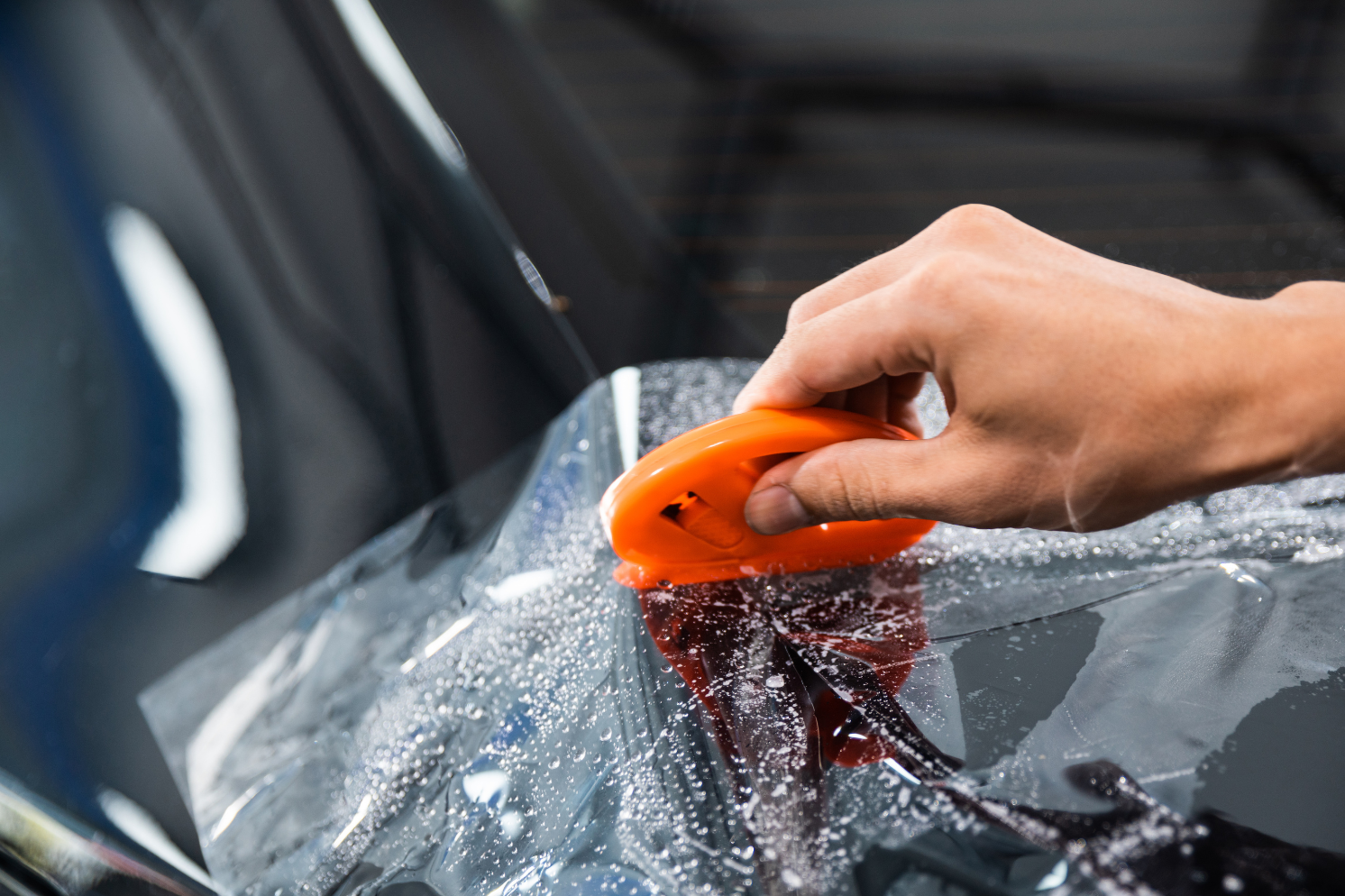 A black Mercedes with clear protective film on the hood in an indoor shop.