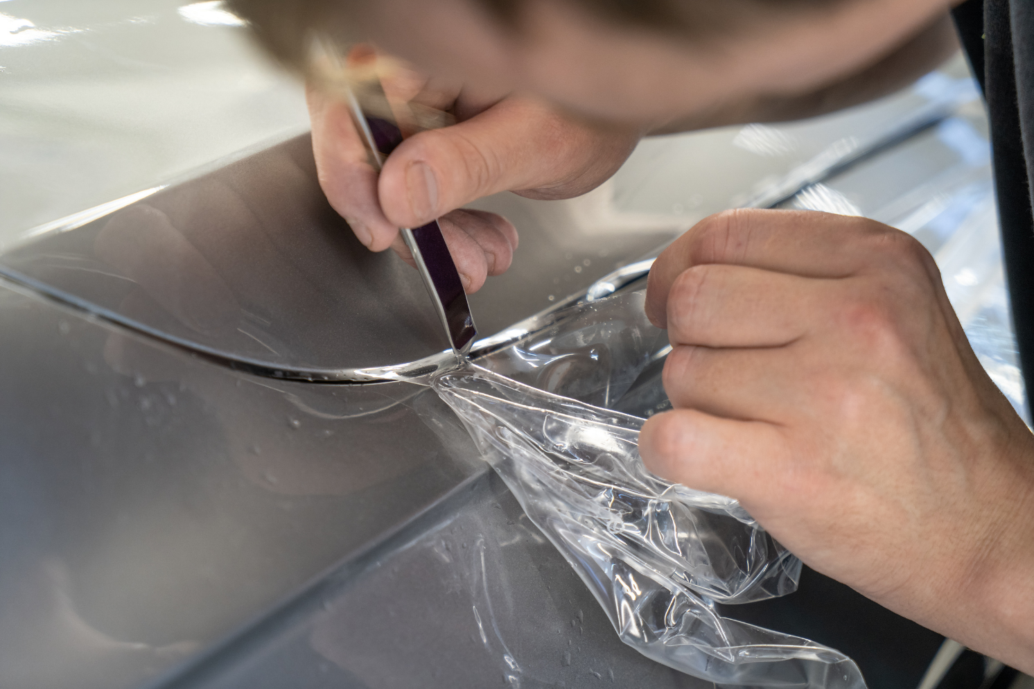 Person wearing gloves cleaning the inside of a car window with a blue cloth.