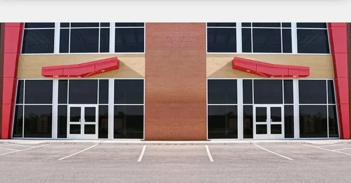 Two-story commercial building with red accents and large windows. Entrance doors and parking area visible.
