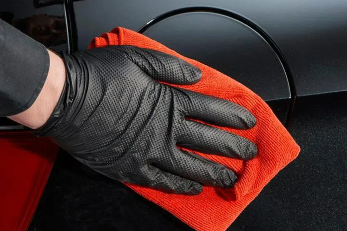 A person wearing black gloves is cleaning a car with an orange cloth.