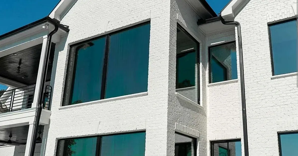 White brick house with large teal-tinted windows; black trim and gutters.