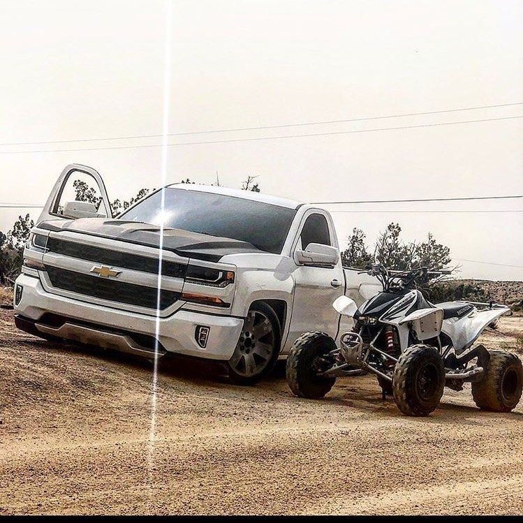 A white truck is parked next to a atv on a dirt road.
