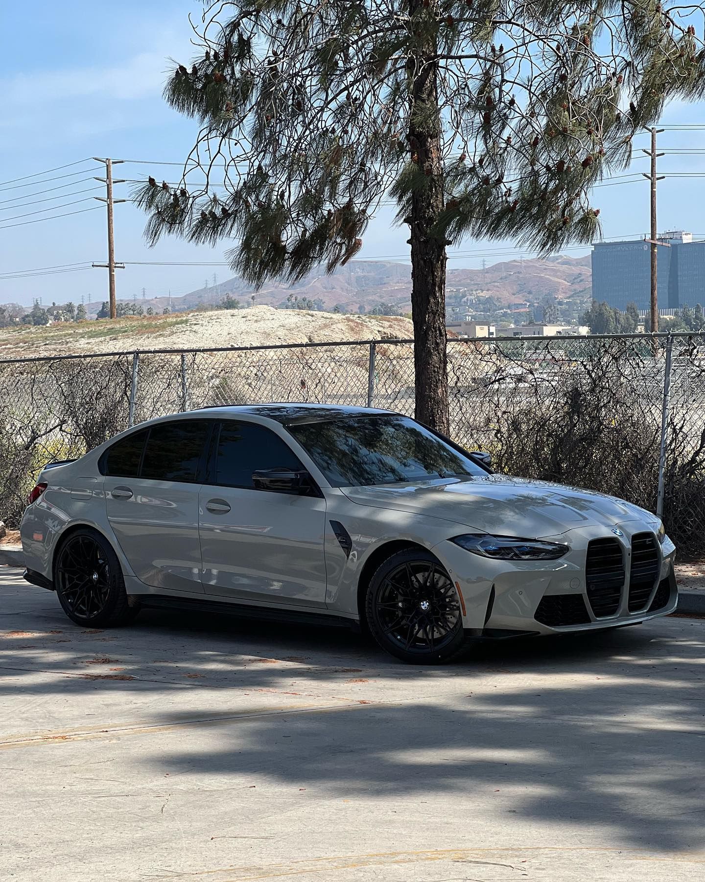 A white bmw m3 is parked in a parking lot next to a tree.