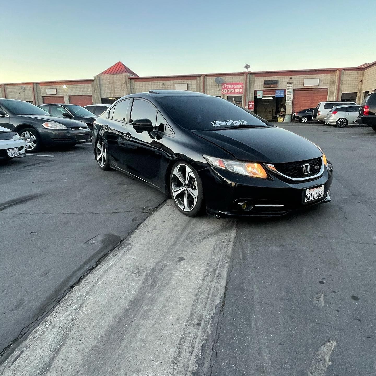 A black car is parked in a parking lot with other cars.