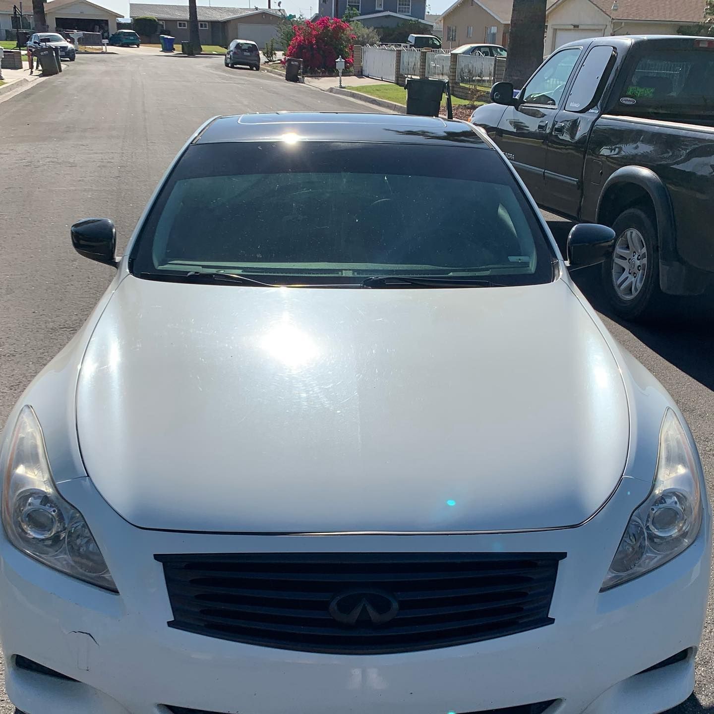 A white infiniti car is parked on the side of the road