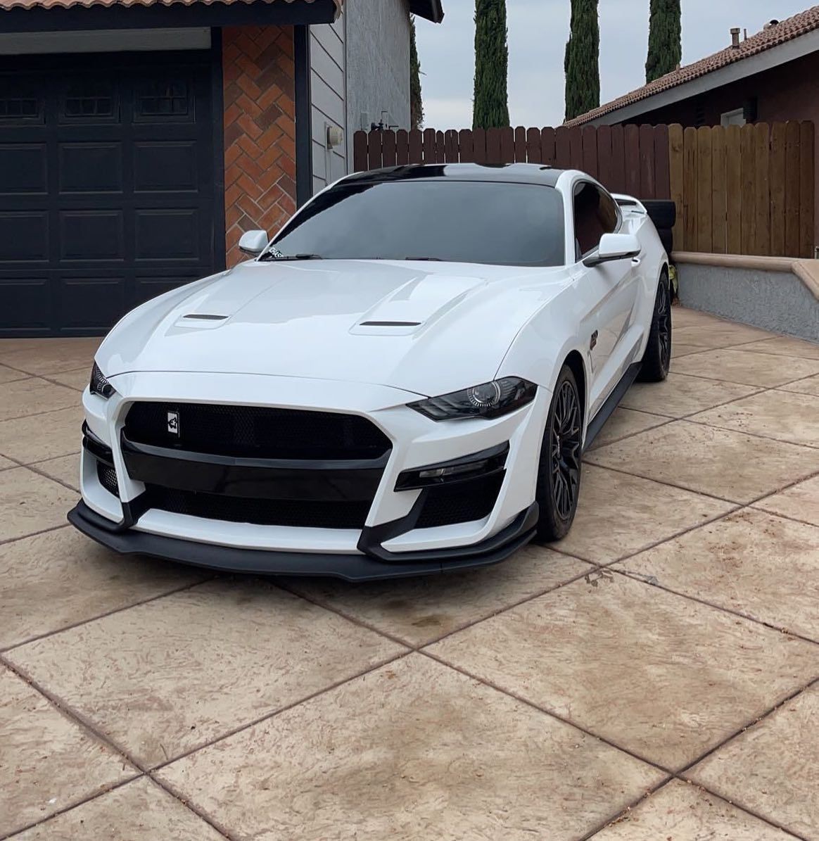 A white mustang is parked in front of a garage