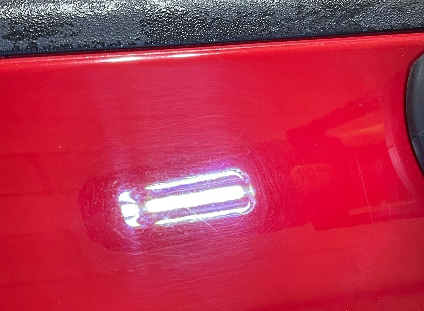 A close up of a red car with a reflection of a light on it.