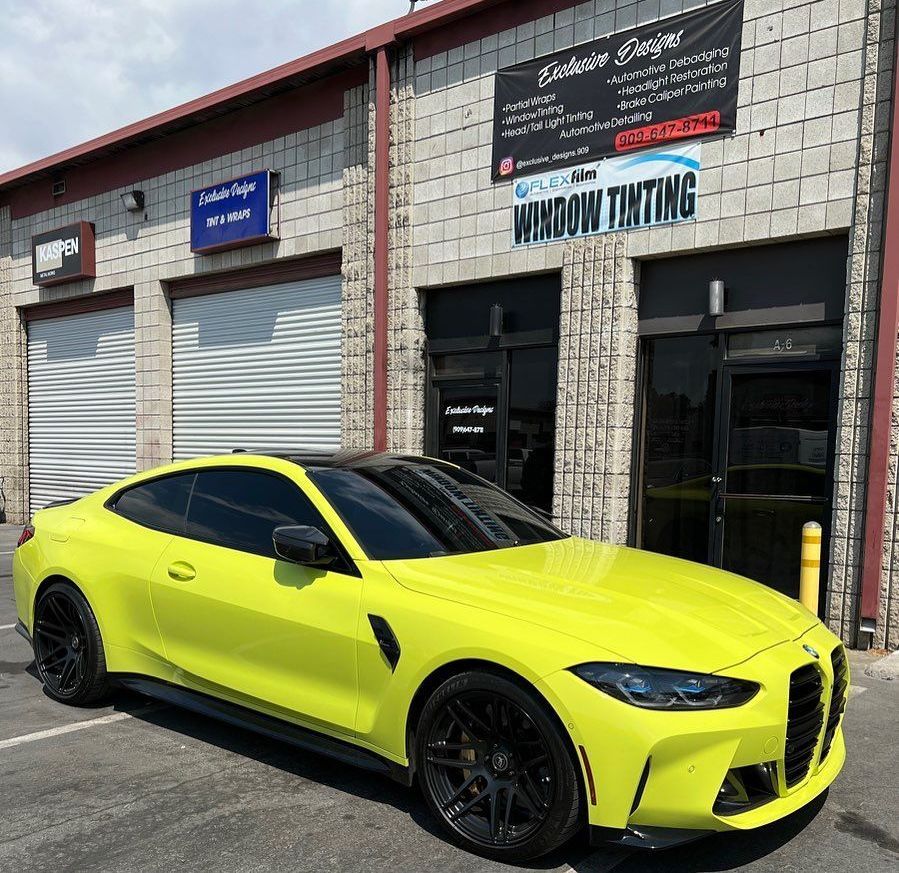 A yellow bmw m4 coupe is parked in front of a building.