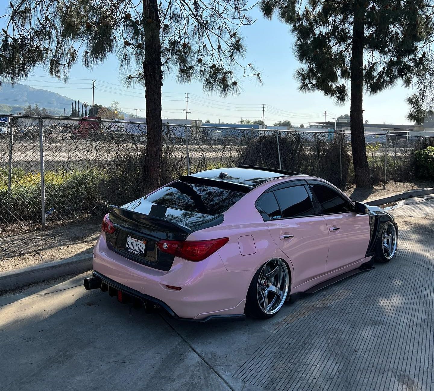 A pink car is parked in a parking lot with trees in the background.