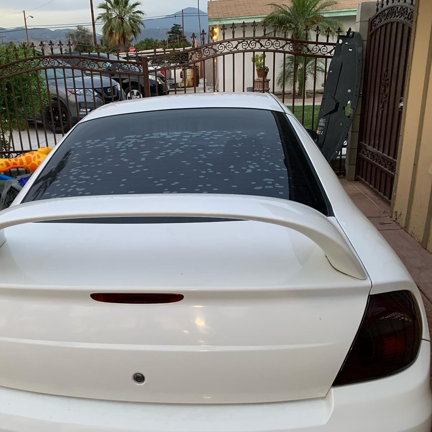 A white car is parked in front of a fence