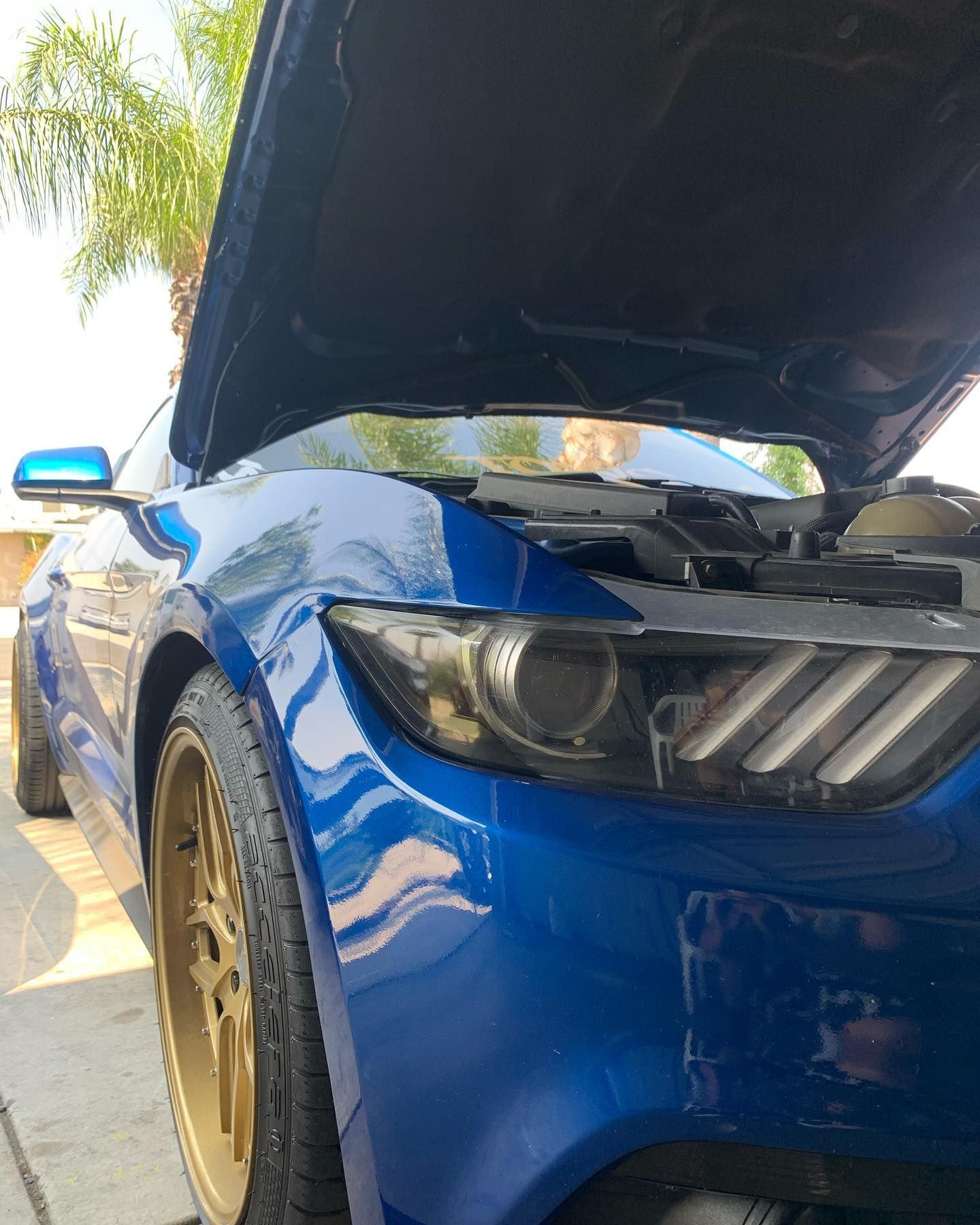 A blue car with the hood up is parked on the side of the road.