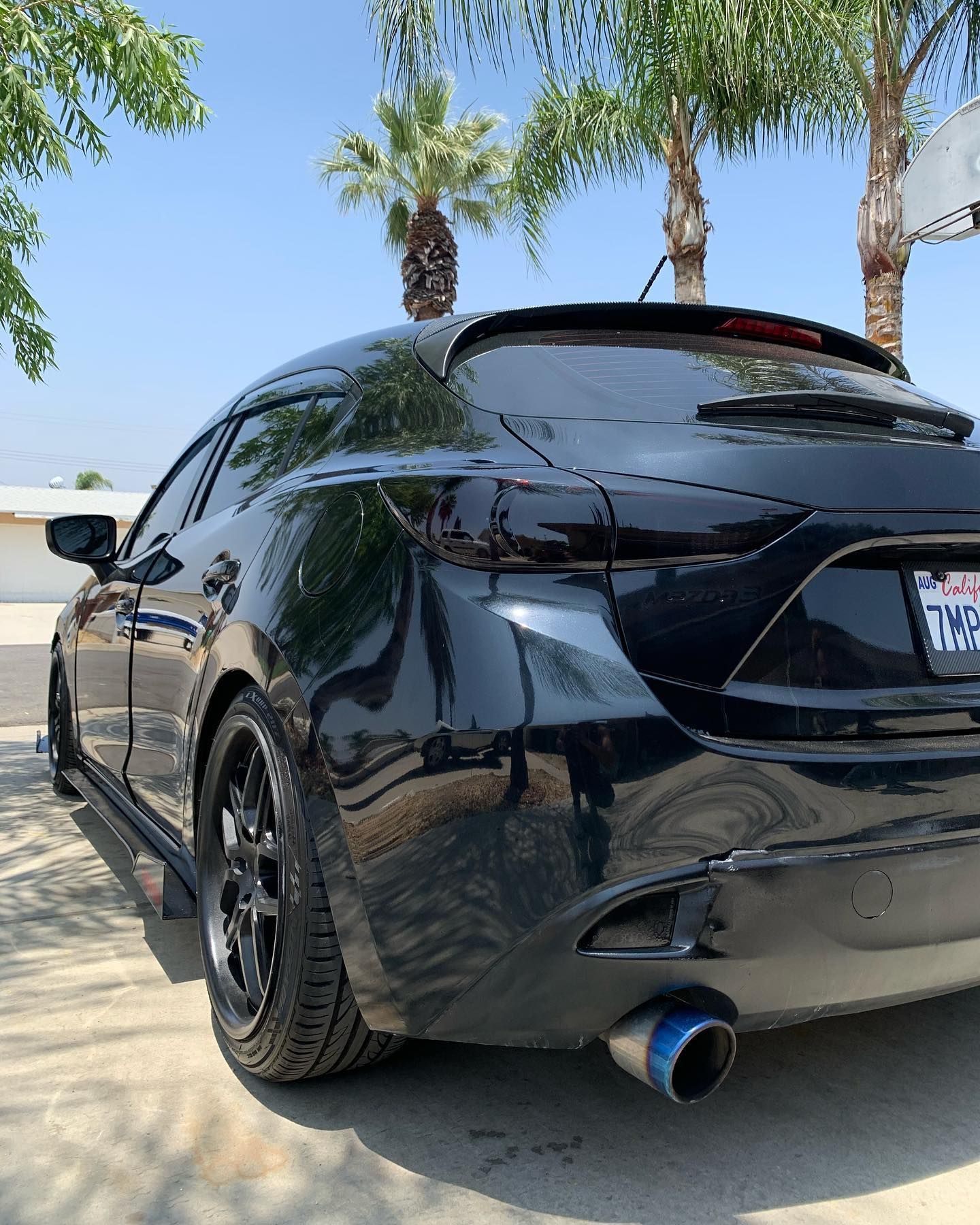 A black car is parked in a driveway with palm trees in the background.