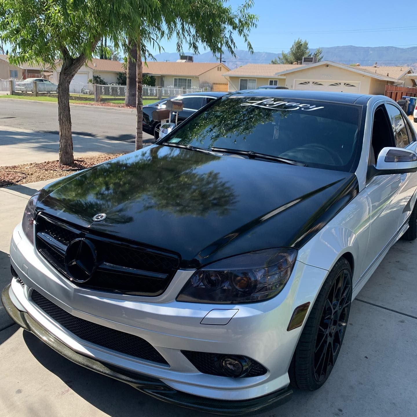 A silver car with a black hood is parked on the side of the road