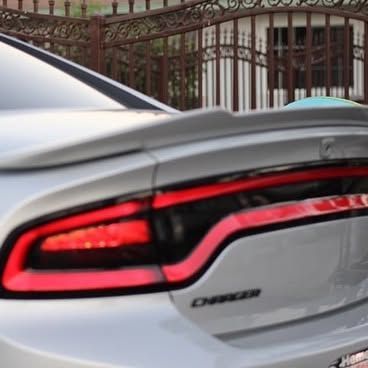 A silver dodge charger is parked in front of a fence