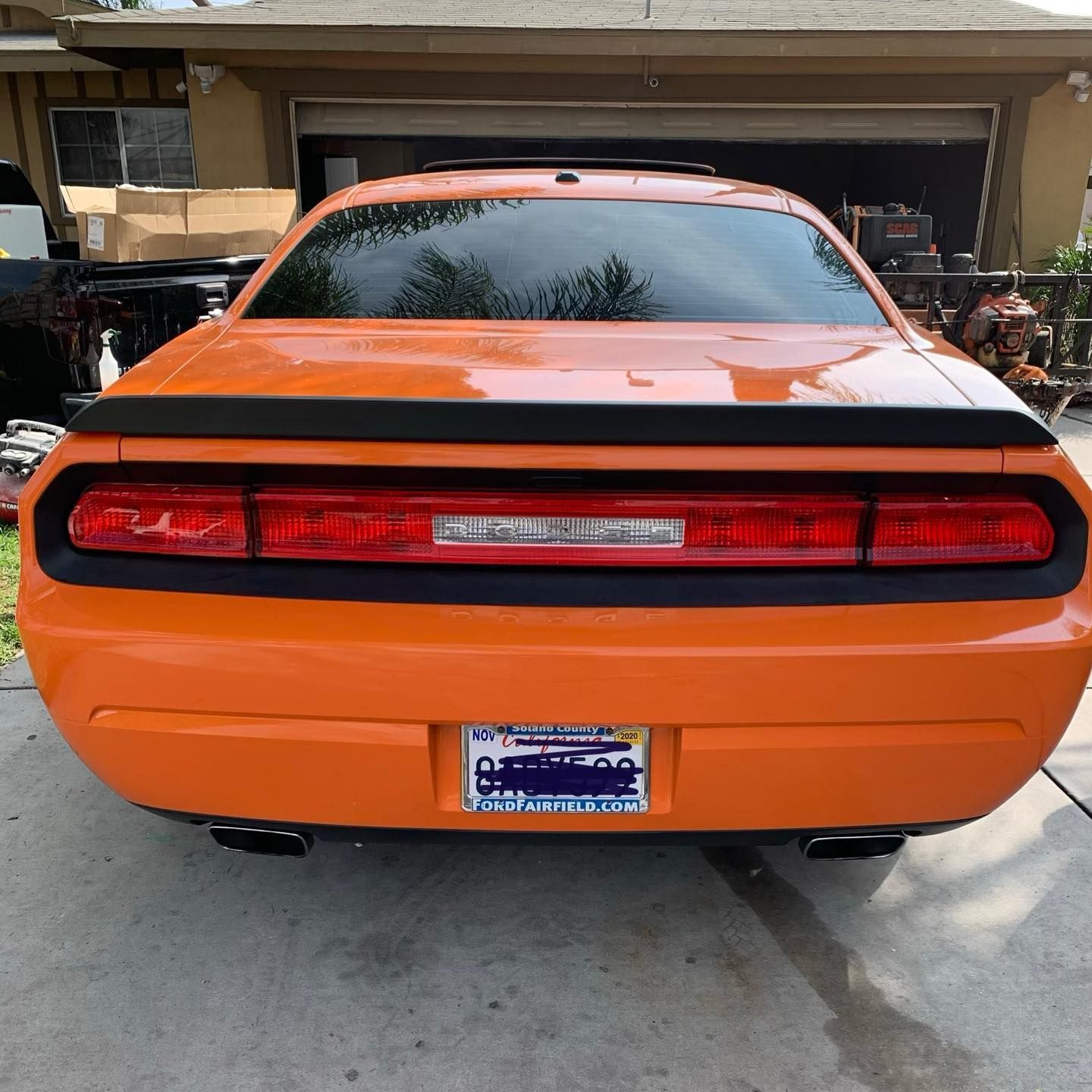 An orange dodge challenger is parked in front of a garage