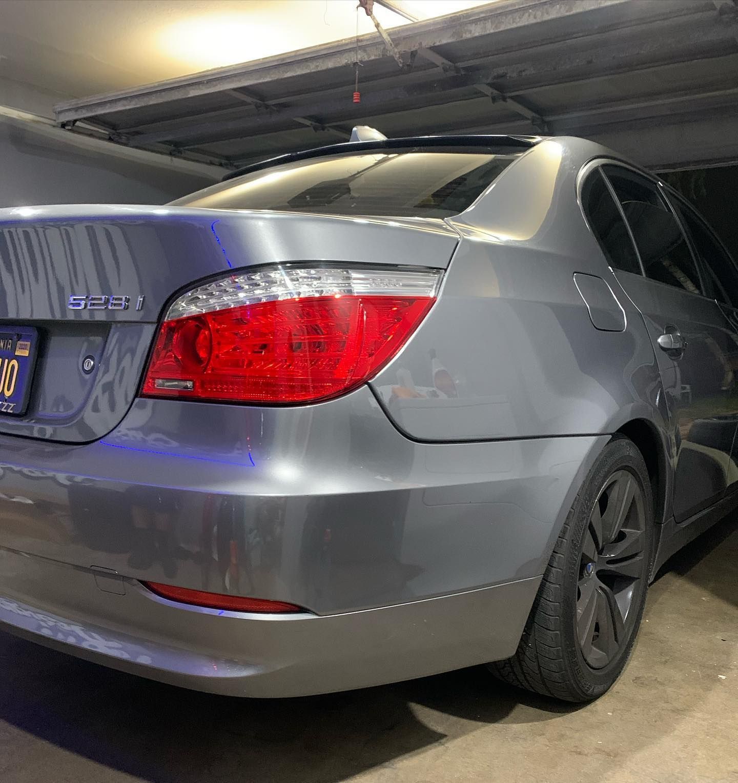 A gray car with a red tail light is parked in a garage.