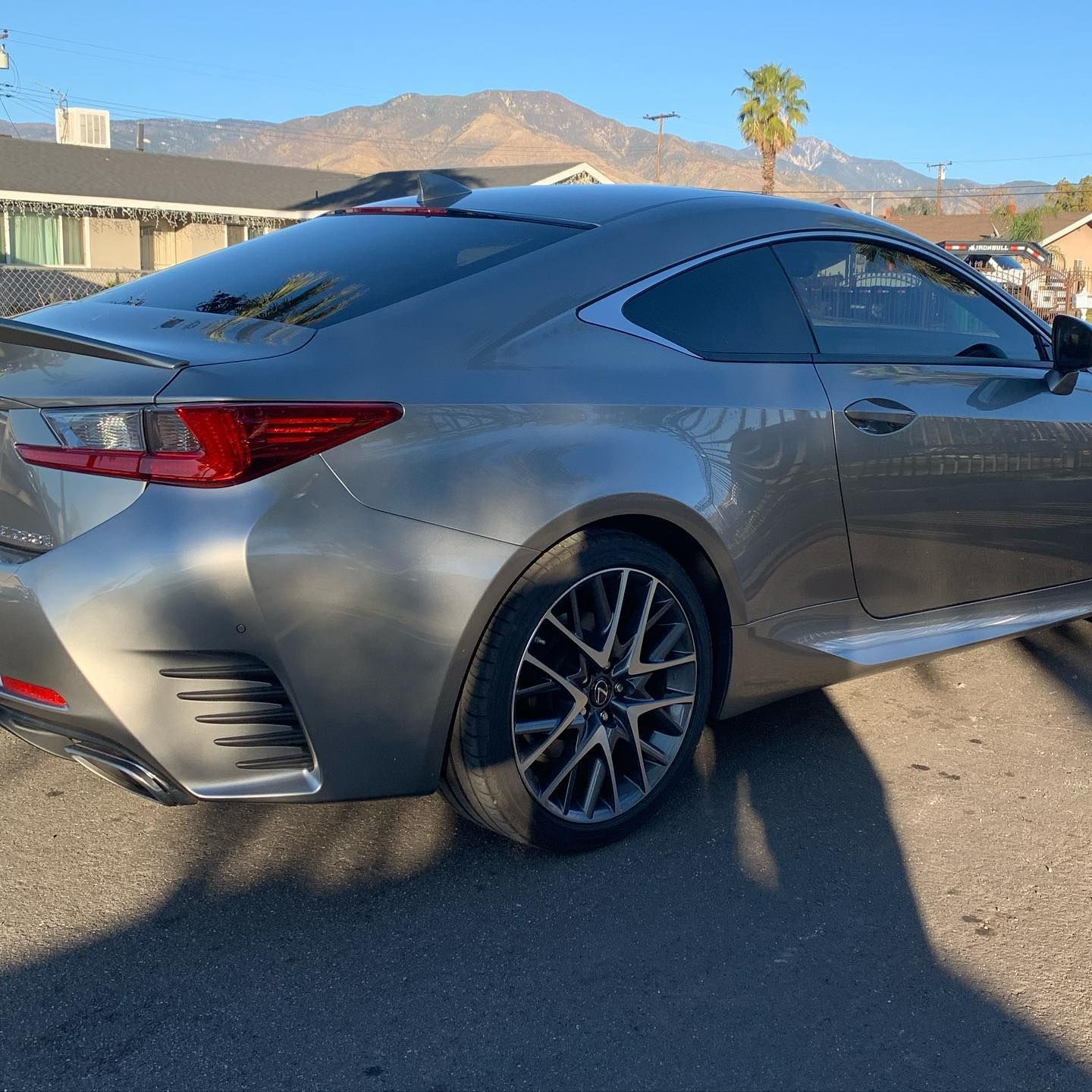 A silver sports car is parked in a parking lot with mountains in the background.