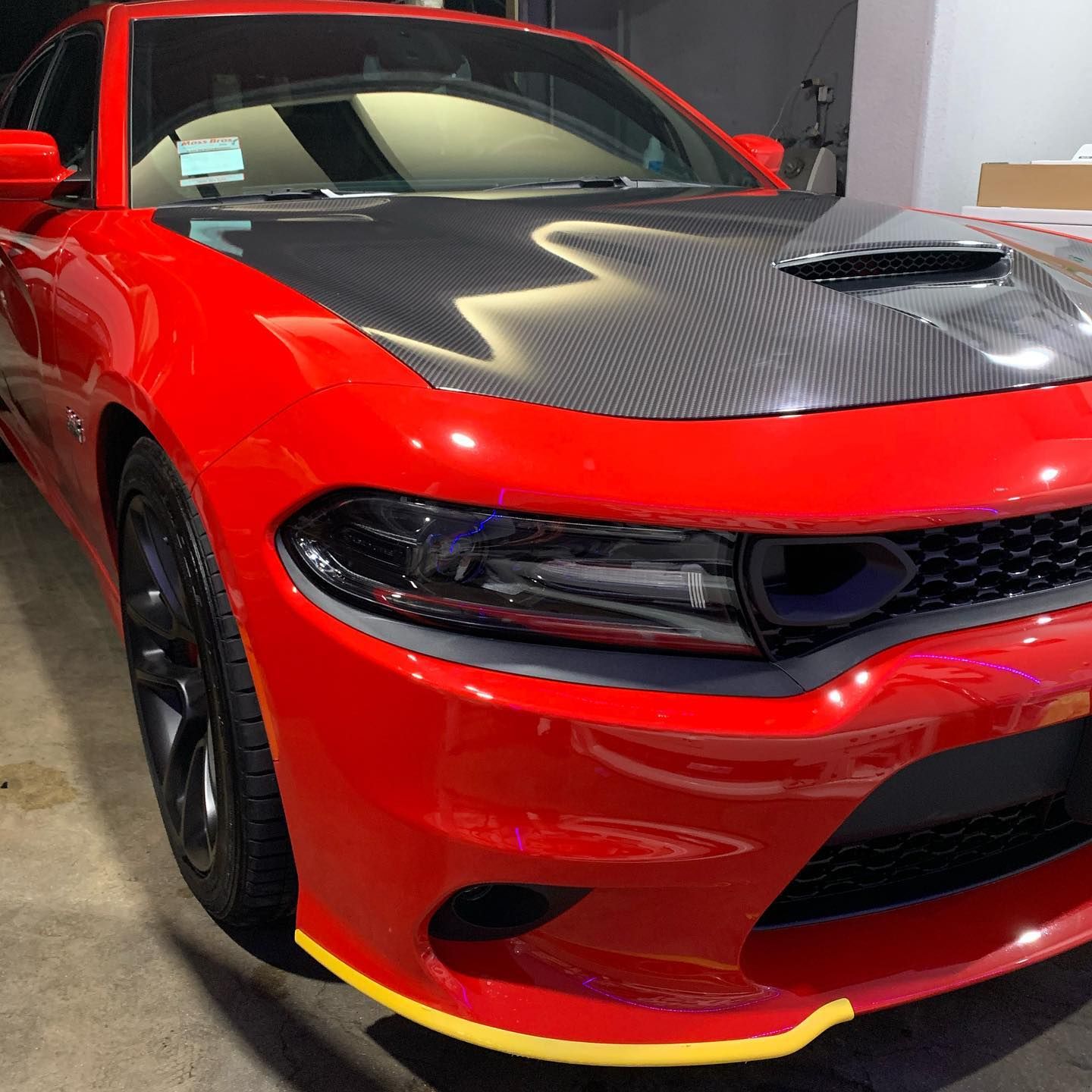 A red car with a carbon fiber hood is parked in a garage