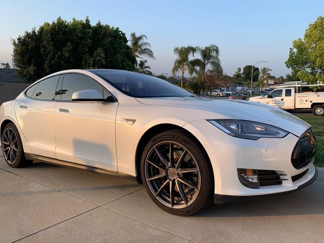 A white tesla model s is parked on the side of the road.