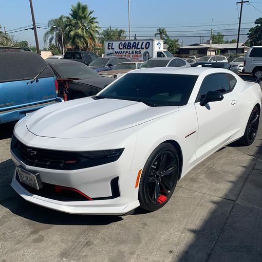 A white car is parked in front of a truck that says el caballo