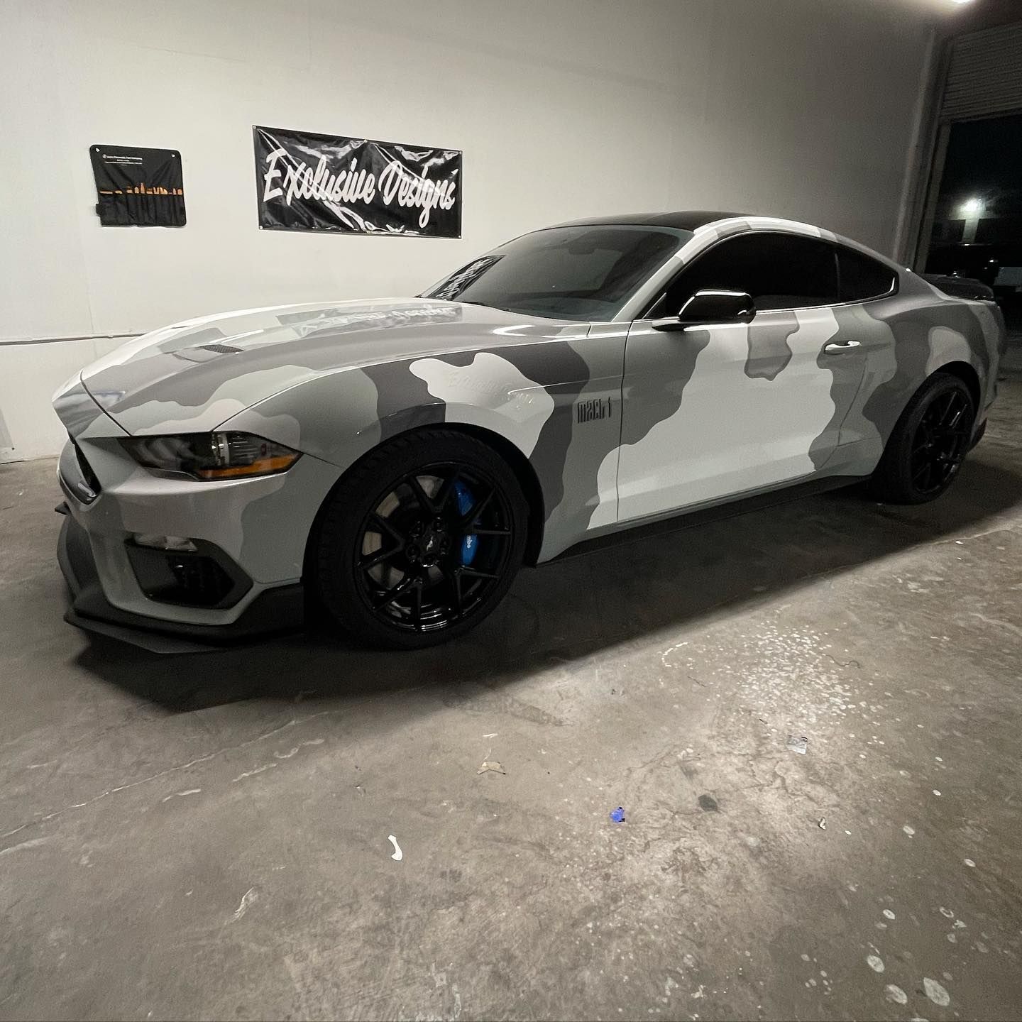 A white mustang with a camouflage wrap is parked in a garage.