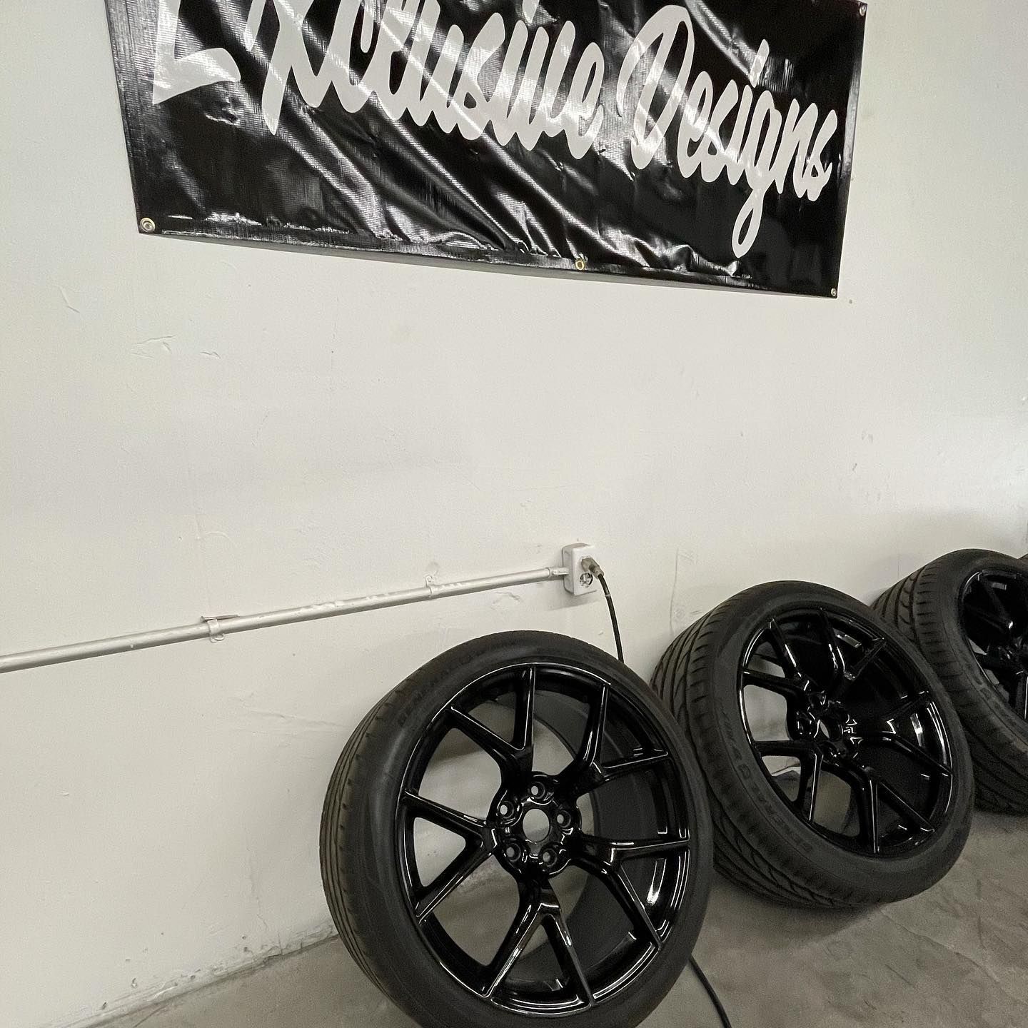 A group of black wheels and tires are sitting under a sign that says racing designs.