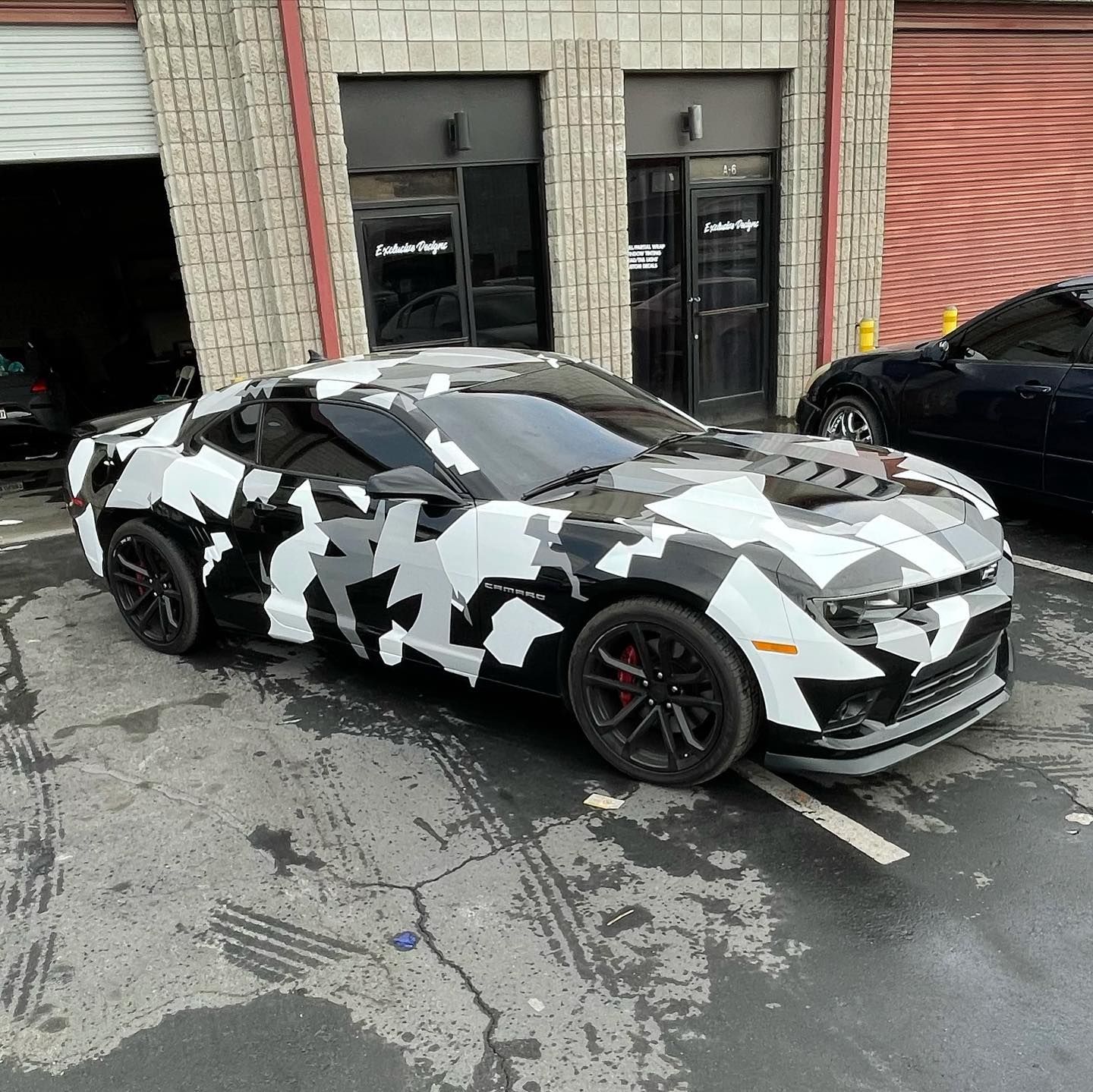 A black and white camouflage car is parked in front of a building.