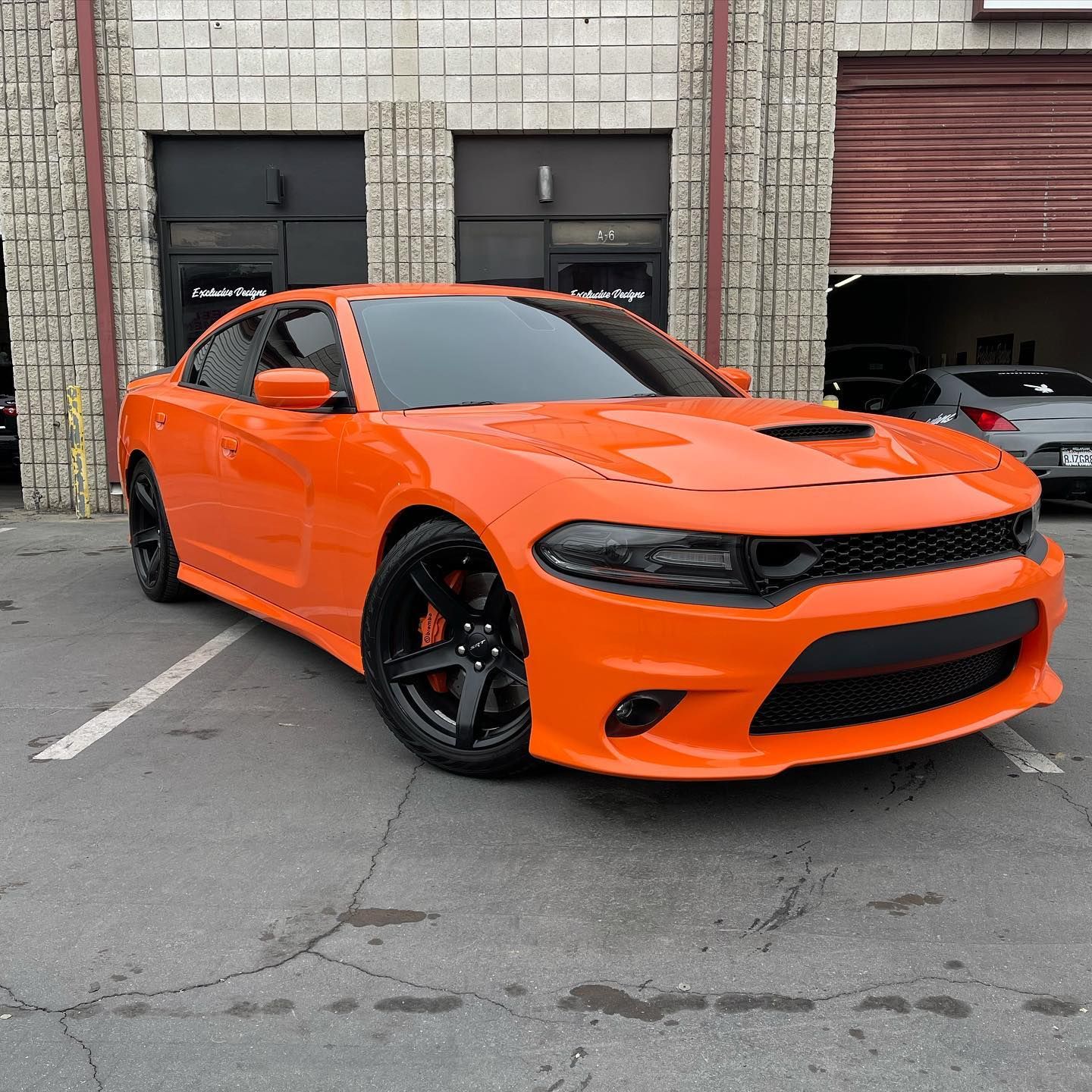 An orange dodge charger is parked in a parking lot in front of a building.